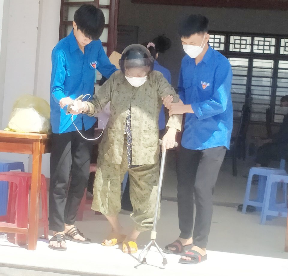 Đoàn viên xã Tam Thăng (TP.Tam Kỳ) giúp đỡ người già ra về khi tiêm vắc xin Covid-19 xong.