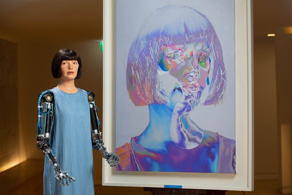 Ai-Da bên cạnh bức chân dung tự họa tại triển lãm cá nhân ở Bảo tàng thiết kế London ngày 31.8.2021. Ảnh: PA Wire