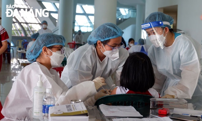 Các nhân viên y tế thực hiện liệu pháp tâm lí cho một em nhỏ khi tiêm vì sợ đau.