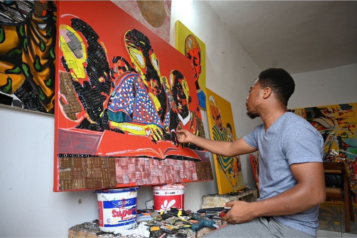 Nghệ sĩ trẻ Mounou Desire Koffi và tác phẩm nghệ thuật được tô vẽ nên từ rác thải điện tử. Ảnh: AFP