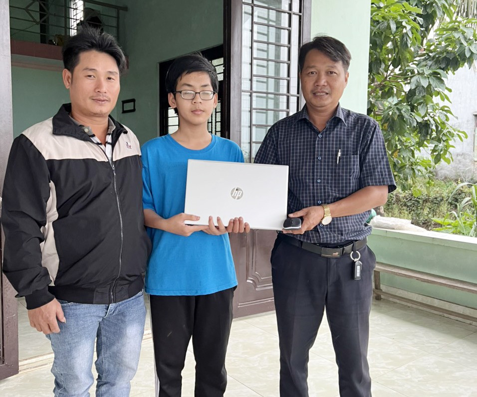 Thầy Phạm Công Hà (bên phải) tặng máy tính xách tay cho học sinh vượt khó tại Điện Bàn. Ảnh: T.N