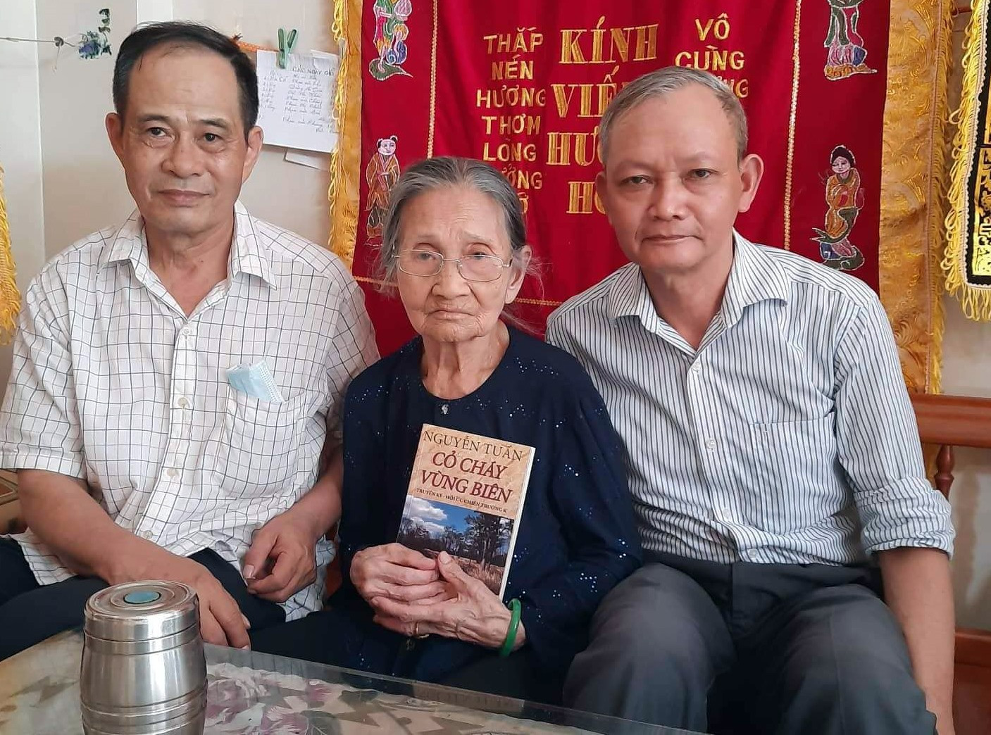 Tác giả Nguyễn Tuấn (bìa trái) tặng sách “Cỏ cháy vùng biên” cho gia đình liệt sĩ Phạm Văn Chung.