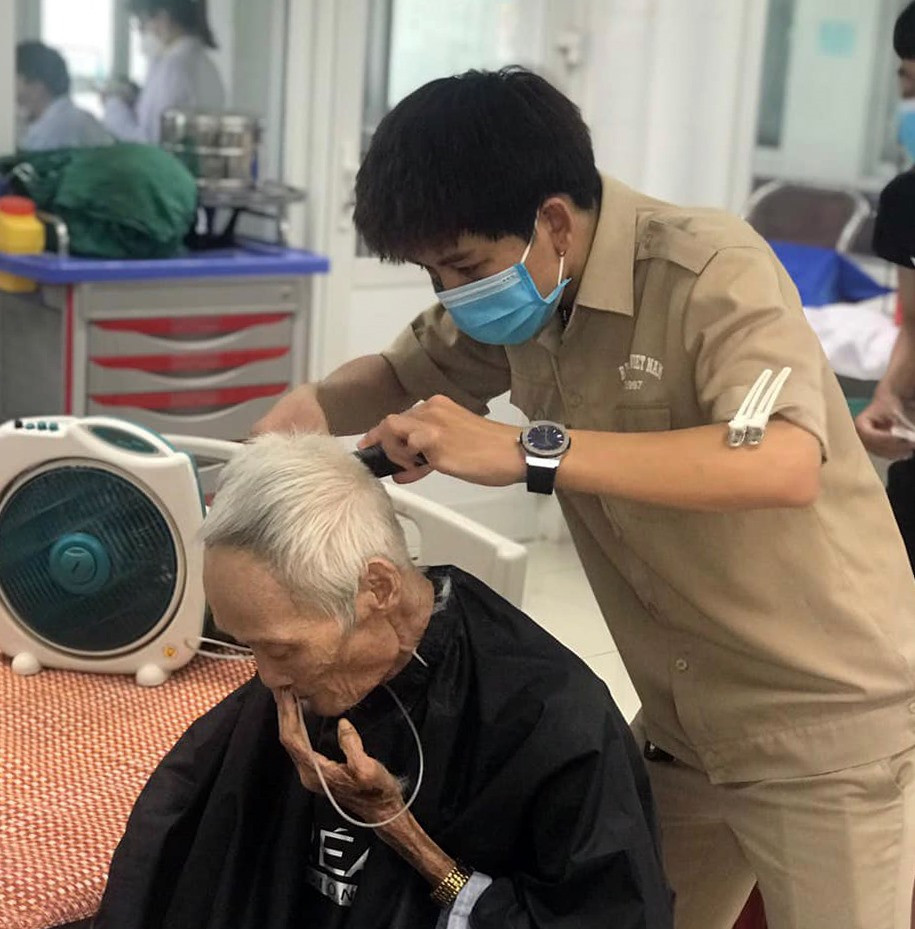 Những tình nguyện viên đang giúp một bệnh nhân cao tuổi tải đi mái tóc đã quá dài, gây khó cho quá trình điều trị bệnh.