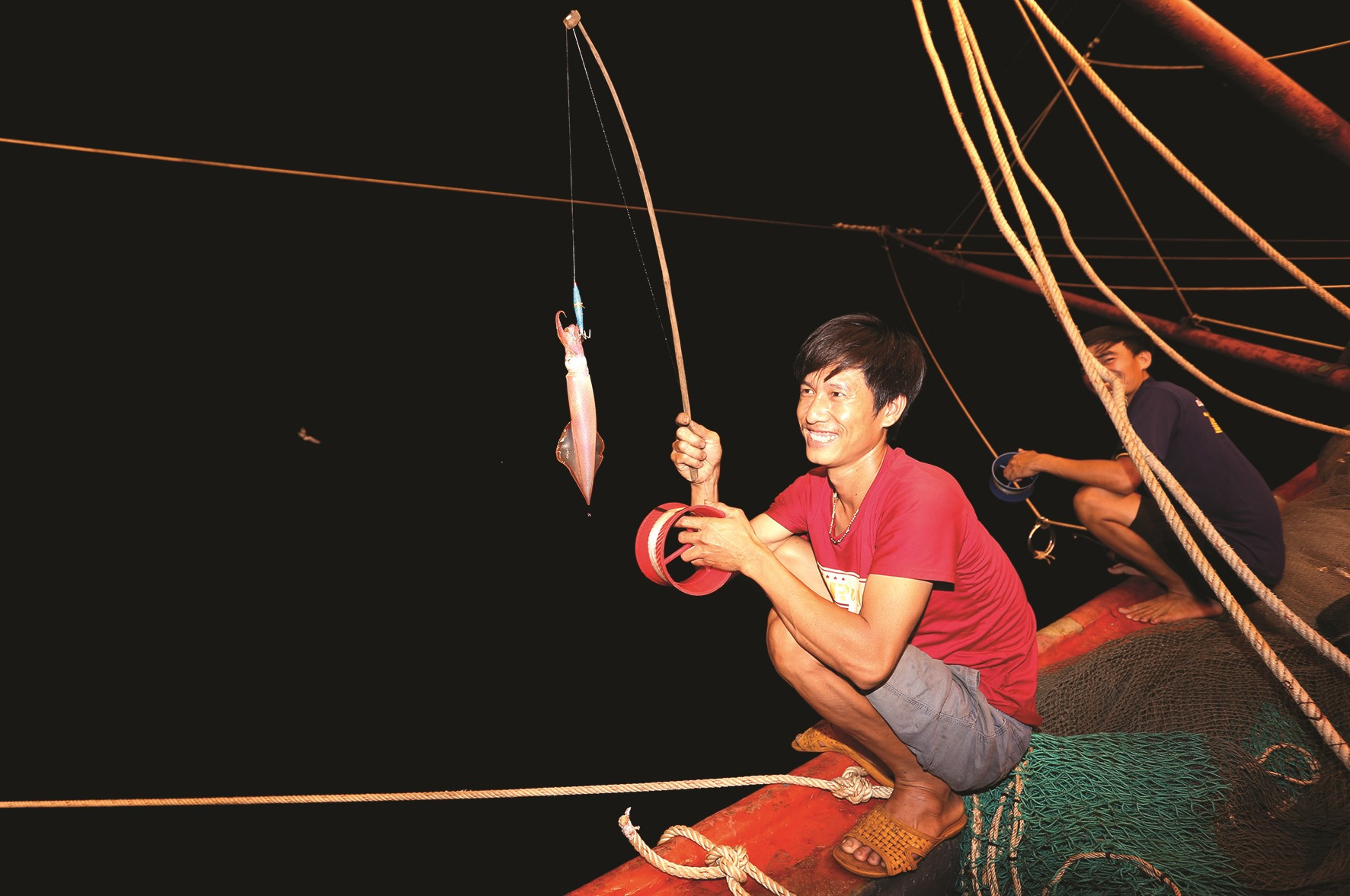 Ngư dân Nguyễn Tấn Lực (Tam Tiến, Núi Thành) kéo một con mực mắc câu lên boong tàu.