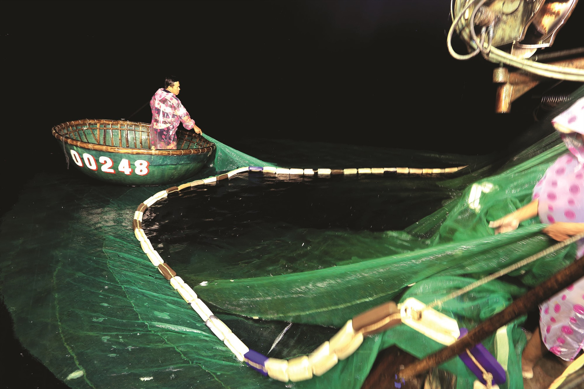 Ông Trần Văn Nở dùng thuyền thúng đi phía ngoài giữ phao nổi trên mặt nước ngăn cá thoát ra ngoài.