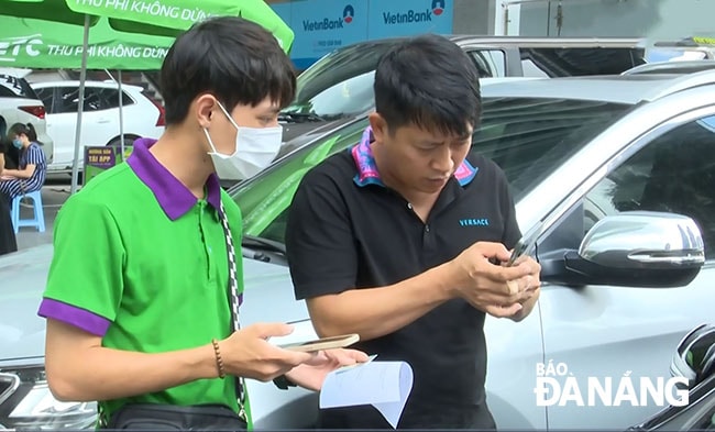 Nhân viên Công ty TNHH Thu phí tự động (VETC) (bên trái) hỗ trợ lái xe dán thẻ thu phí tự động không dừng. Ảnh: PHƯƠNG UYÊN