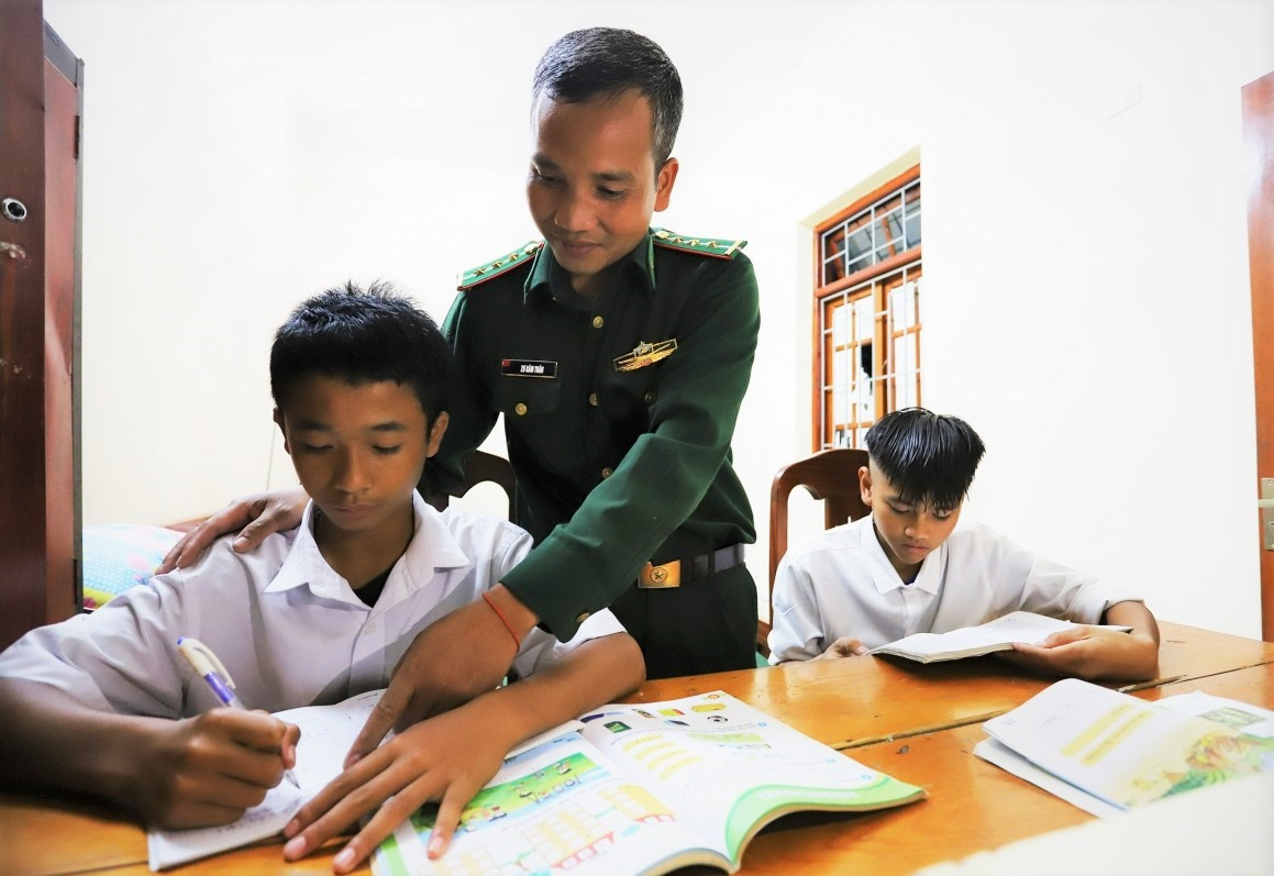 Thượng úy Zơrâm Thân hỗ trợ dạy học cho con nuôi Alăng Chi và Zơrâm Dũng. Ảnh: Đ.N