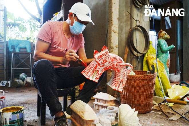 Anh Lê Ngọc Thuận đang sơn màu cho tượng mèo từ củi lũ. Ảnh: NAM ĐỊNH