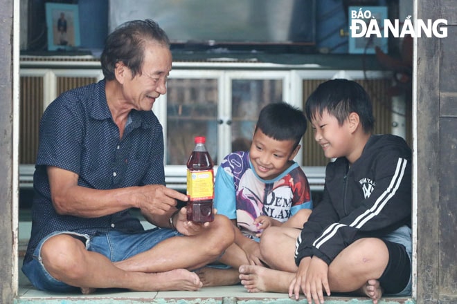 Ông Trần Ngọc Vinh kể cho cháu ngoại nghe về nghề làm mắm truyền thống của gia đình. Ảnh: TIỂU YẾN