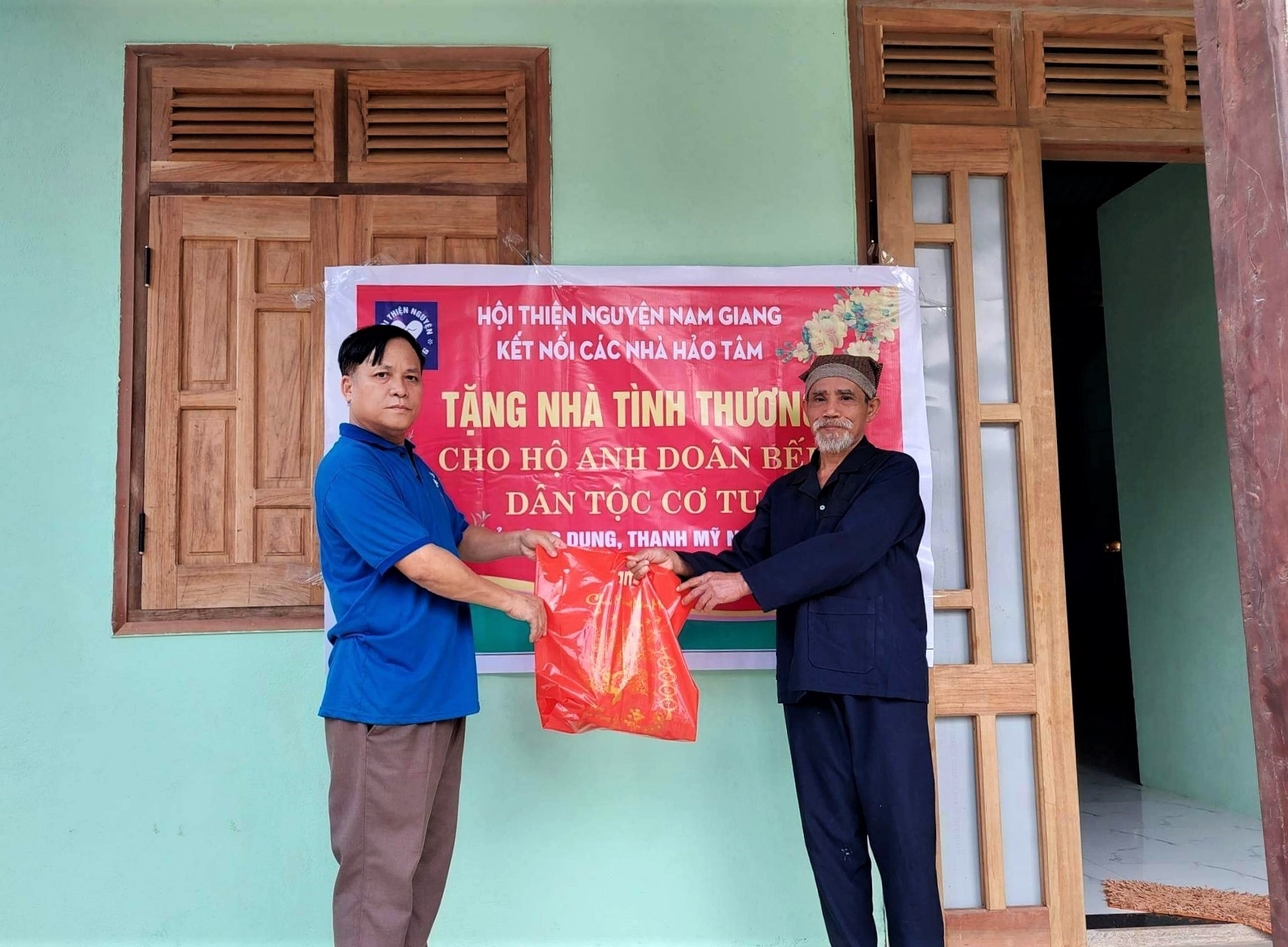 Ông Doãn Bếp (bên phải) đón nhận món quà tết động viên từ đại diện Hội Thiện nguyện Nam Giang trong ngày bàn giao ngôi nhà tình thương. Ảnh: Đ.N