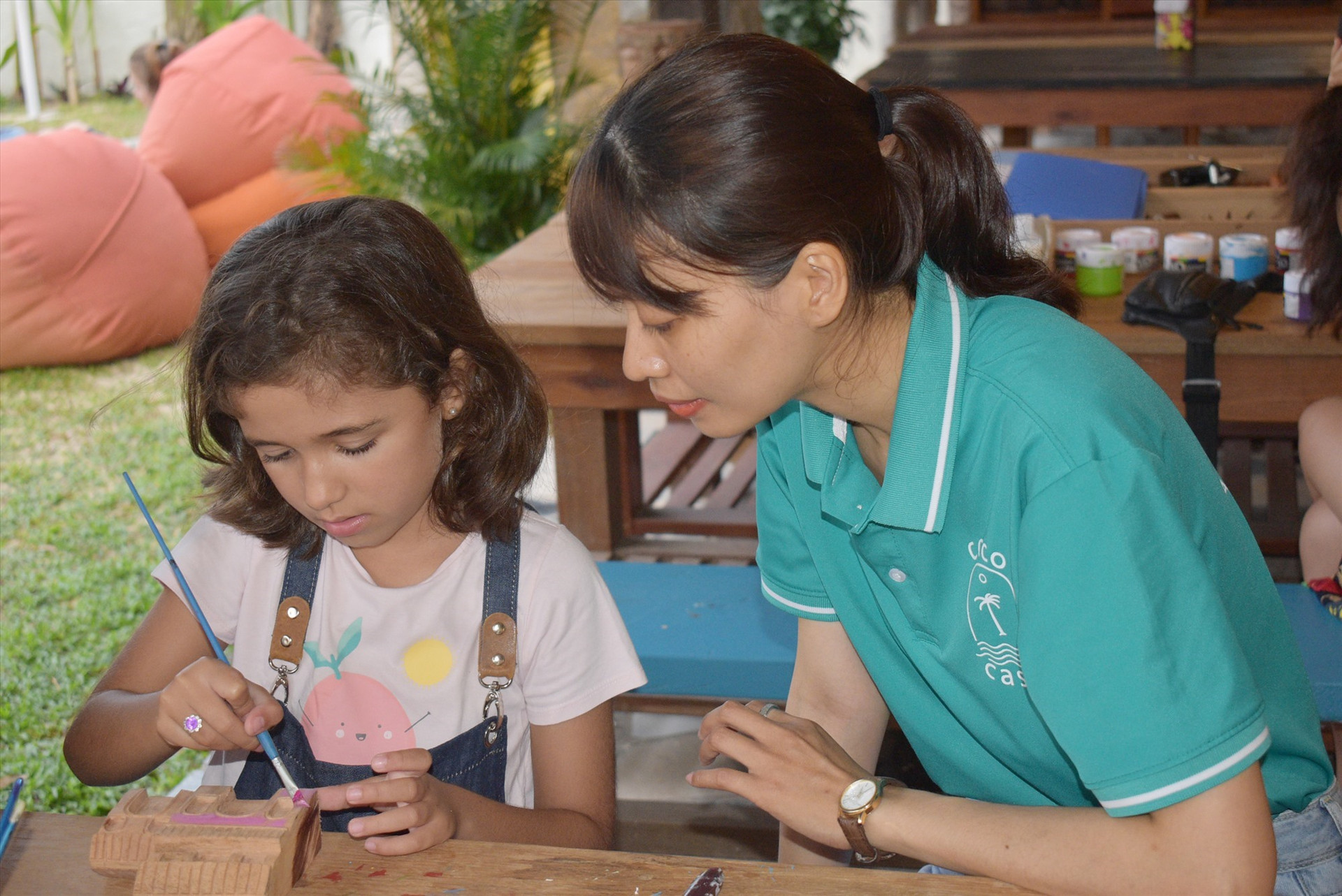 A foreign child learns how to colour a wooden miniature Chua Cau