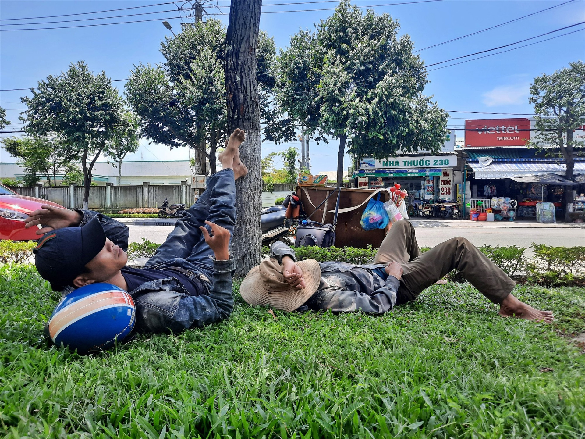 Ông Ngô Đình Dương (bên phải) tận dụng bãi cỏ, bóng râm trước Bệnh viện Đa khoa Quảng Nam để “trốn” nắng nóng. Ảnh: Đ.T
