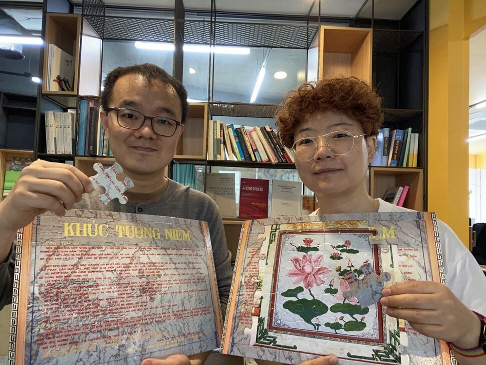 Tổng thư ký Kwon Hyeon-woo (trái) của Quỹ Hòa bình Hàn-Việt và nhà hoạt động Choi Hyeon-jin giơ cao dòng chữ trên Đài tưởng niệm làng Hami và hình ảnh bông hoa sen xếp hình cho khách tham quan triển lãm tư liệu. Ảnh: Theo Hani.co.kr