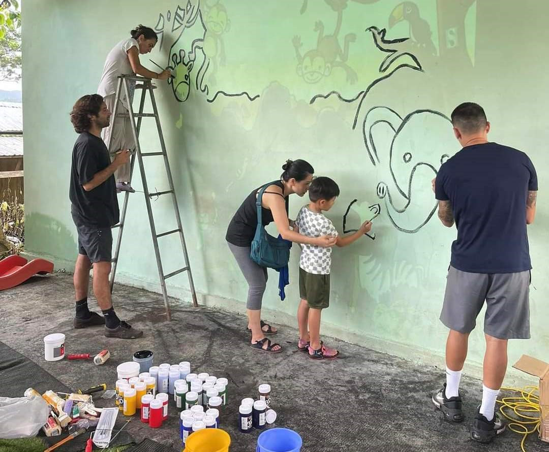 Các tình nguyện viên nước ngoài và trẻ em trong làng cùng vẽ tranh bích họa tại điểm trường mới. Ảnh: L.T.V