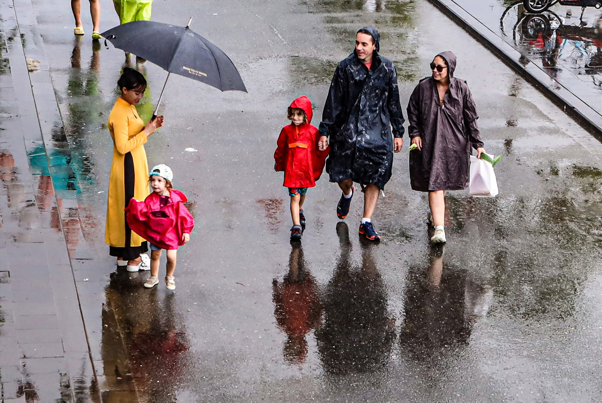 Một gia đình du khách nước ngoài chọn cách mặc áo mưa đi ngắm phố cổ trong mưa để cảm nhận sự tuyệt vời của thời khắc đặc biệt này.