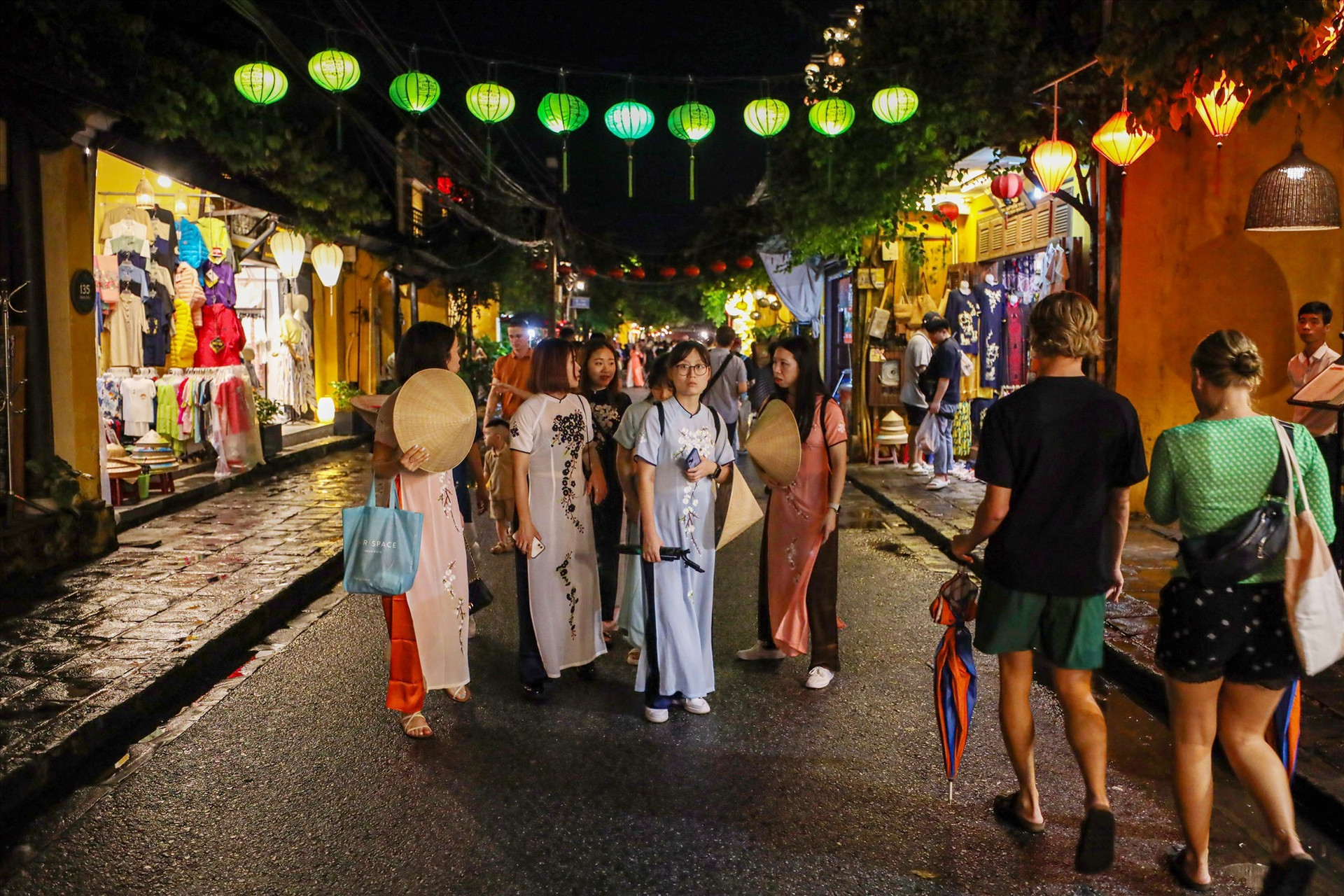International tourists wearing Vietnamese Ao Dai to contemplate Hoi An ancient town.