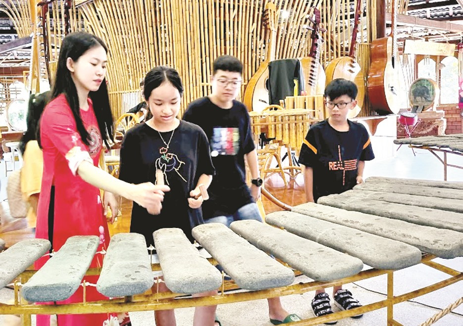 Du khách được hướng dẫn và trải nghiệm chơi nhạc cụ dân tộc ở Làng nghề Trường Sơn. Ảnh: C.N
