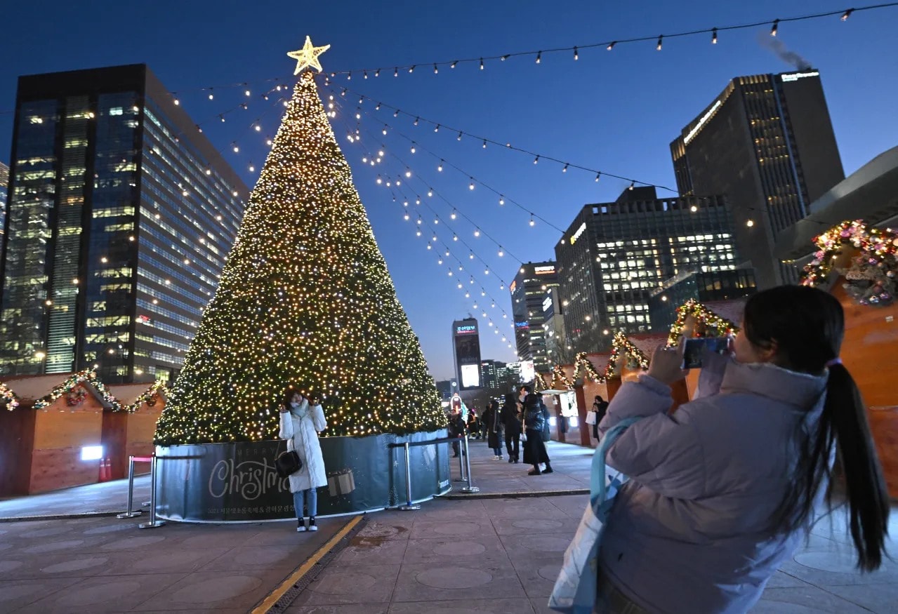 People pose for photos in front of a Christmas tree installation in central Seoul, South Korea, on Dec. 22, 2023. (JUNG YEON-JE/AFP via Getty Images)