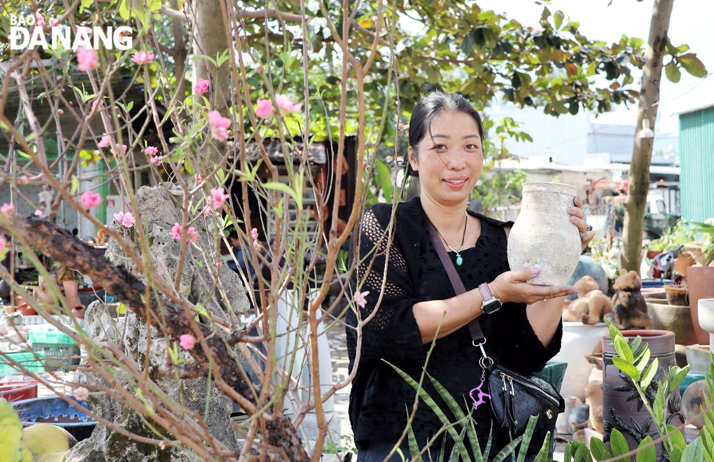 Cô chủ Gốm Nhà Tím giới thiệu một loại gốm giả cổ bên cành đào khoe sắc sớm. Ảnh: NHƯ HẠNH