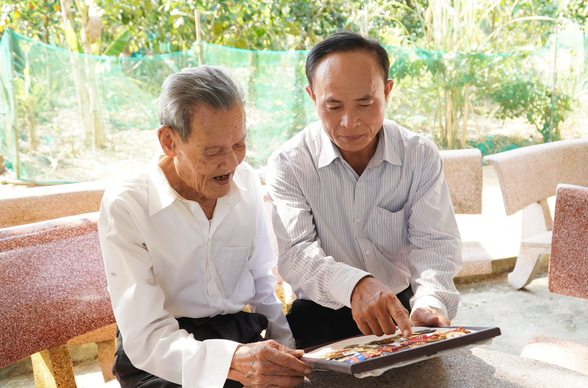 Ông Trần Đình Tư (bên trái) kể về chiến tích và những huân chương được nhận sau chiến dịch Điện Biên Phủ. Ảnh: H.Q
