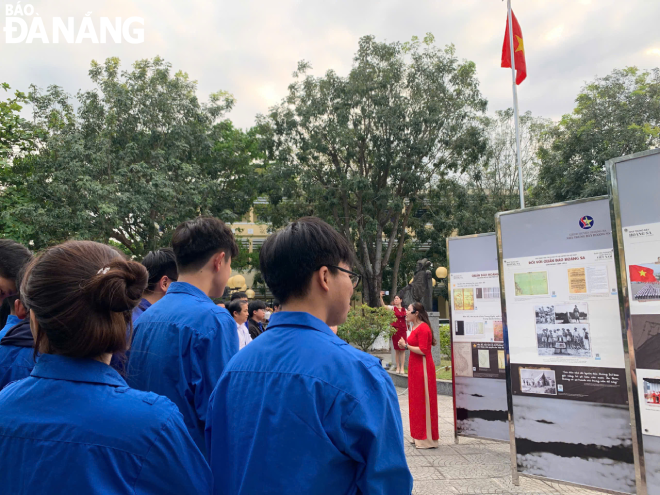 Các em học sinh tham quan triển lãm và nghe thuyết minh viên trình bày về các tư liệu lịch sử.