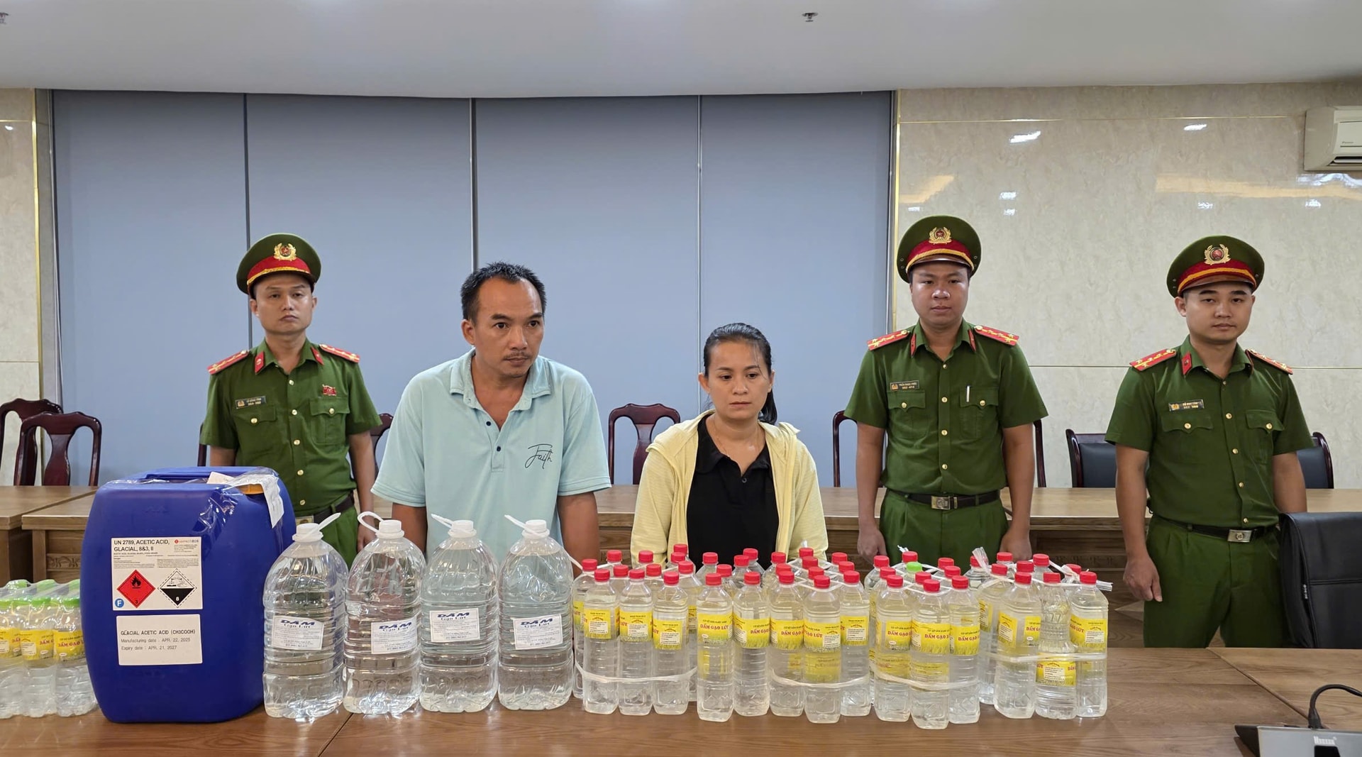 Hai vợ chồng Thanh - Hậu (giữa) cùng tang vật là hóa chất và số giấm giả thành phẩm sắp bán ra thị trường. Ảnh: Công an cung cấp