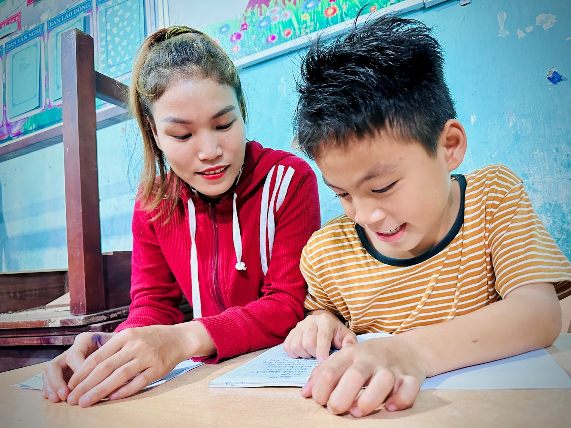 Cậu con trai hỗ trợ mẹ - học viên Cái Mực Thảo đọc lỗi chính tả ngay trong lớp học. Ảnh: ALĂNG NGƯỚC