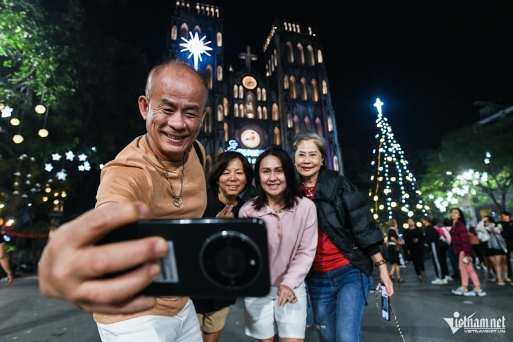 Du khách nước ngoài chụp ảnh kỷ niệm với cây thông Noel tại Nhà thờ Lớn Hà Nội.