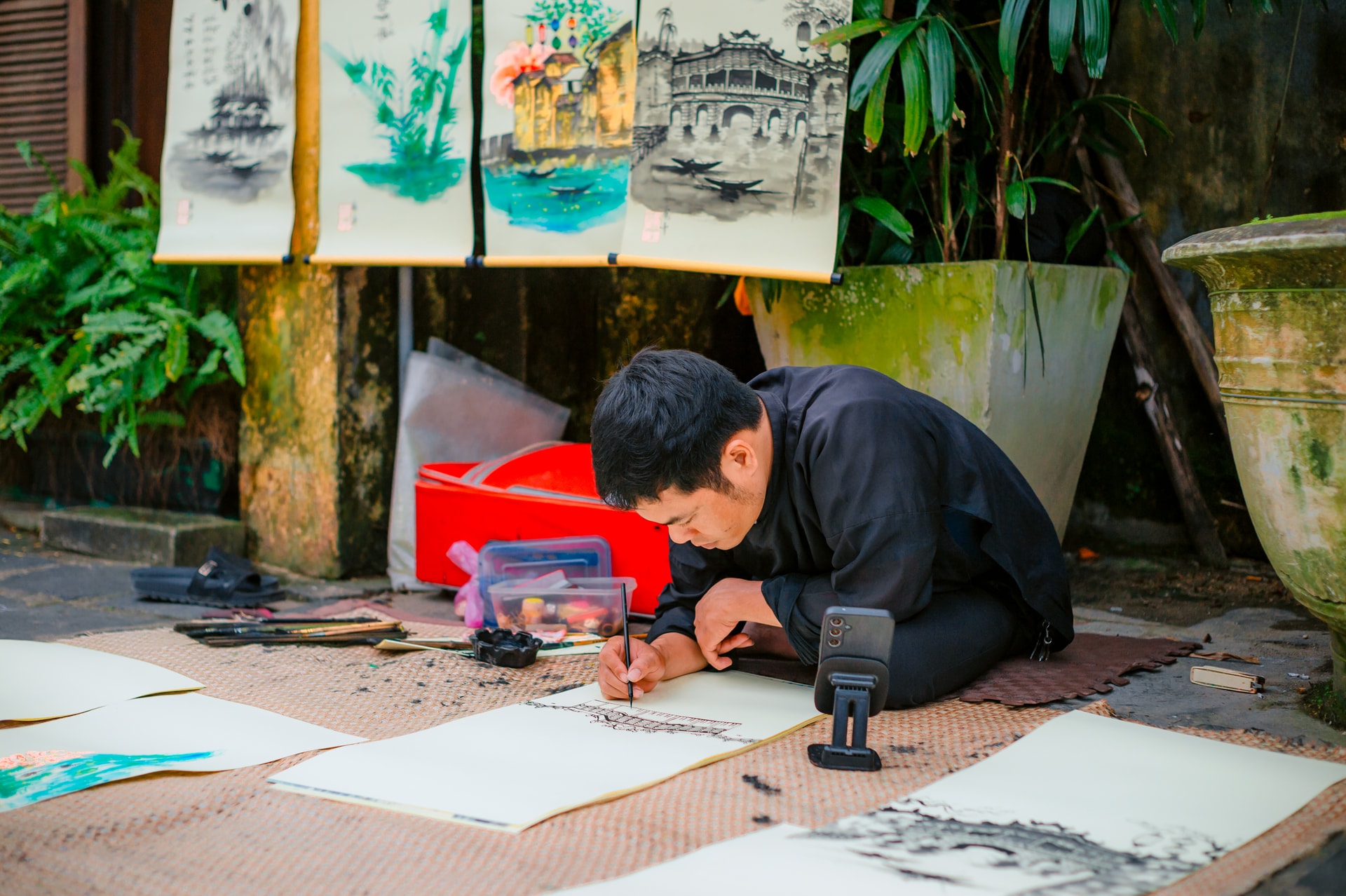 L'artiste, assise sur une natte, peint méticuleusement des lavis d'encre au milieu de la végétation luxuriante de la vieille ville de Hoi An.