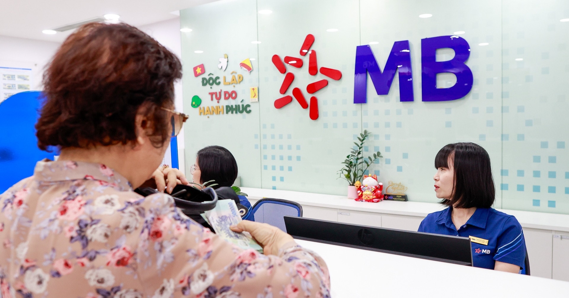Nhân viên ngân hàng đang thực hiện giao dịch với khách hàng cá nhân tại quầy trong bối cảnh lãi suất tăng.
