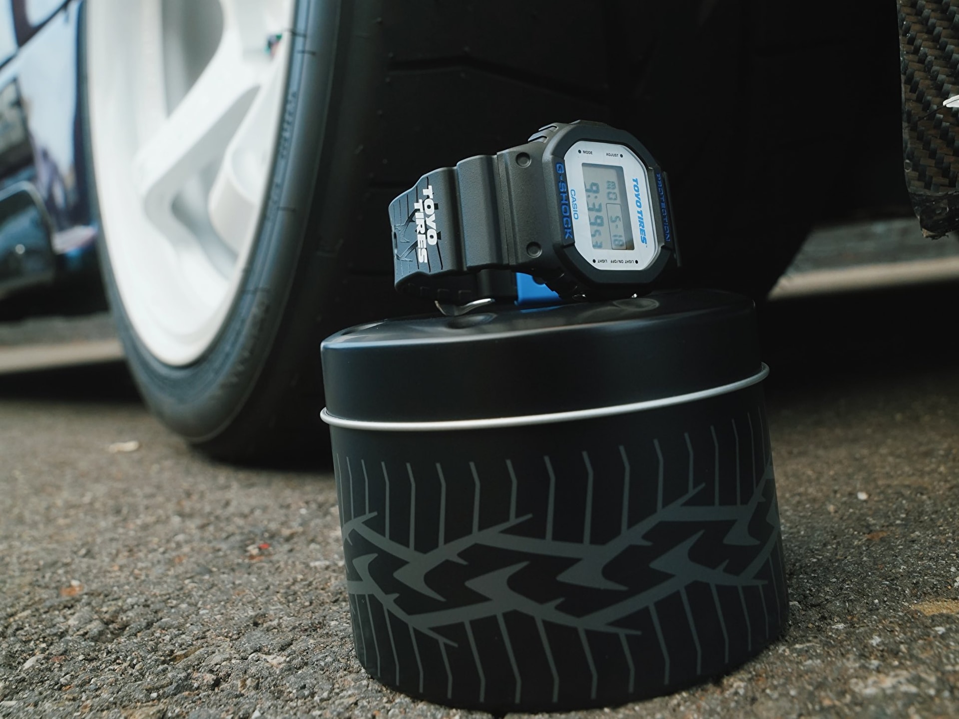 Đồng hồ Casio G-Shock DW5600TT25-1 x Toyo Tires đặt trên hộp thiếc mô phỏng lốp xe