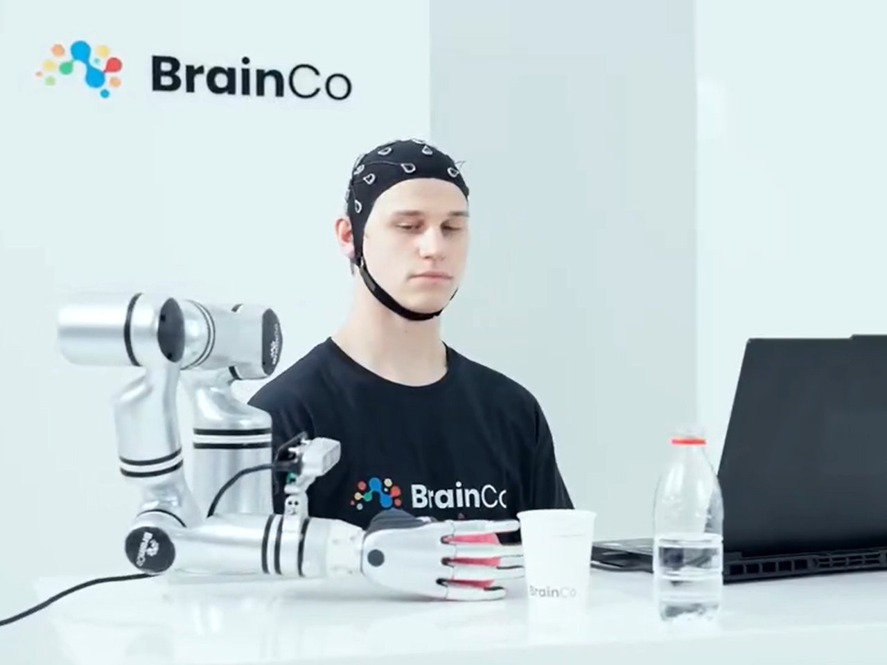 Người dùng công nghệ của BrainCo điều khiển cánh tay robot lấy quả táo bằng ý nghĩ.